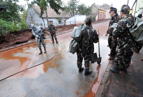 Soldier wearing a chemical protection outfit cleans a street of Devecser