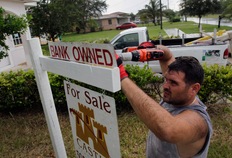 Renzo Salazar places a sign in front of a foreclosed home on Oct. 13 in Miami, Florida; Photo by Joe Raedle/Getty Images