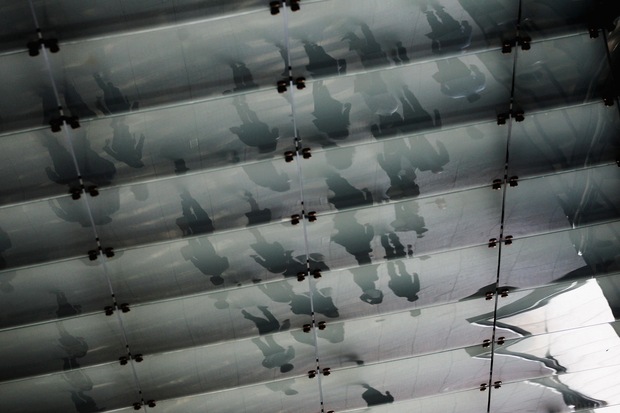 People are reflected in glass as they walk past Goldman Sachs 