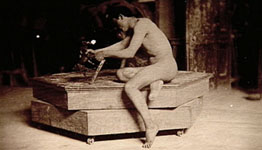 Photograph of Male nude sitting on modeling stand, holding small sculpture of horse, in Pennsylvania Academy studio